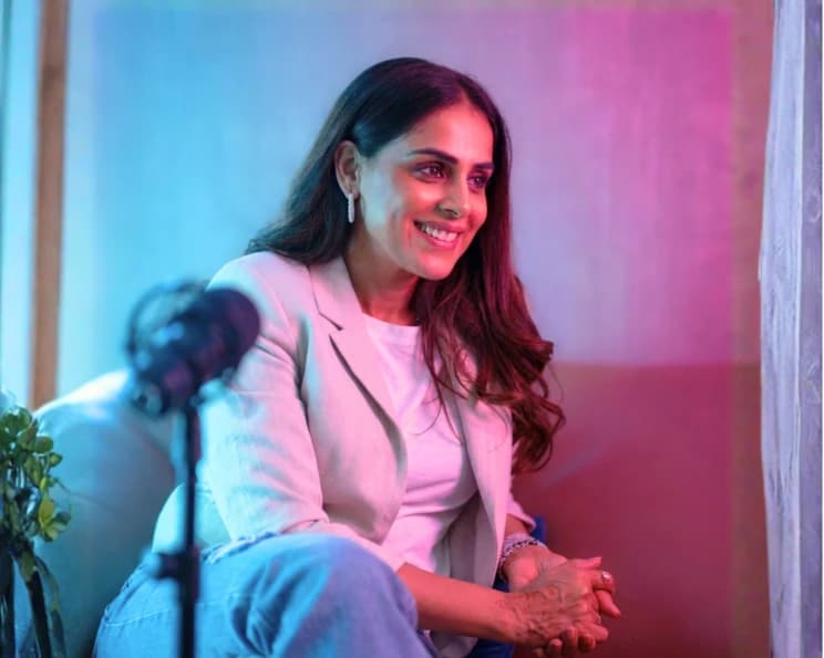 Genelia D’Souza seated at a podcast microphone under magenta lighting